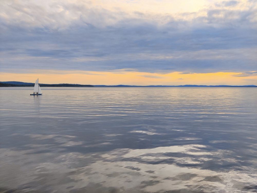 Een zeilboot vaart rustig voorbij de uiterste punt van Långbryggan, honderden meters in het Siljanmeer.