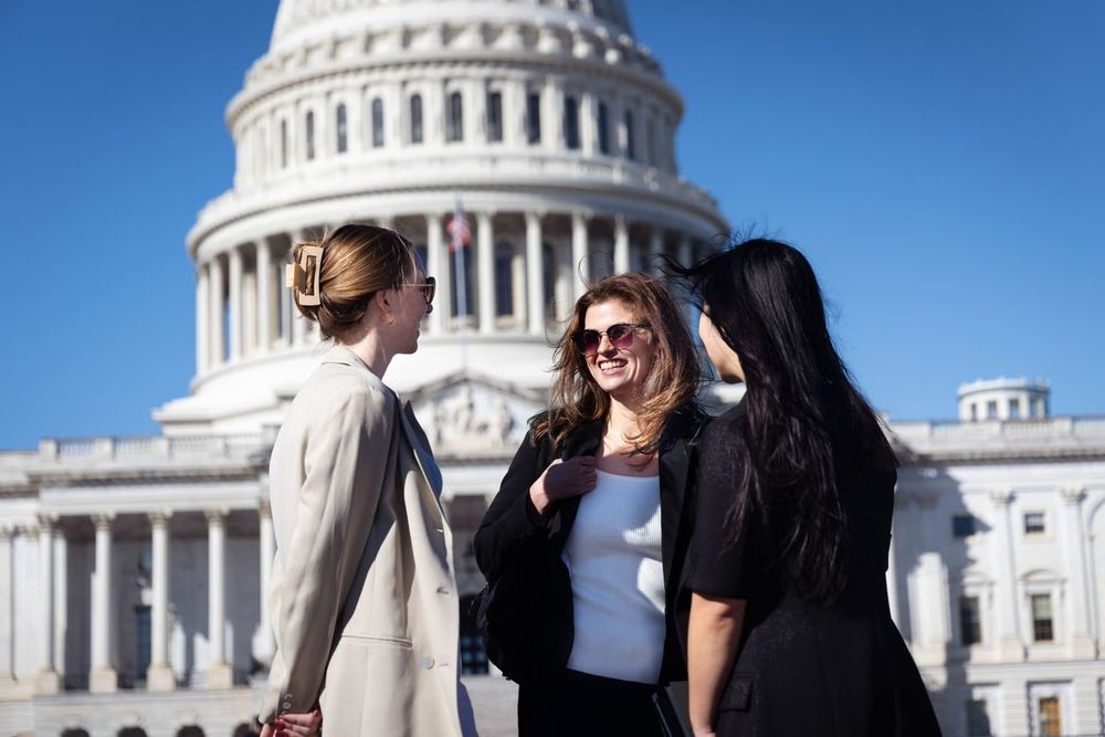 Three people chatting happily in front of the United States Capitol Building on a sunny day.