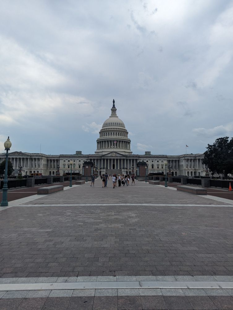 View of the United States Capitol building on a cloudy day, with people walking in the foreground.