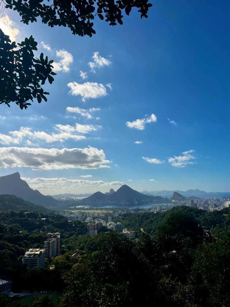 View of Rio de Janeiro with visible landmarks such as Corcovado Mountain and Sugarloaf Mountain, under a clear sky with scattered clouds.
