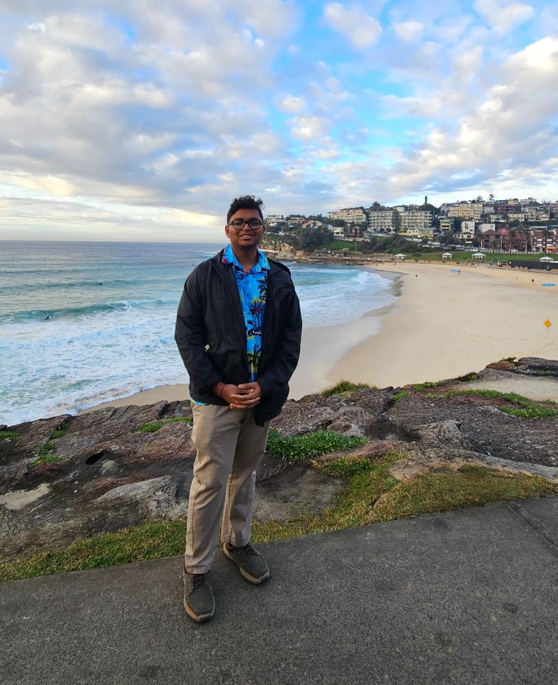 An individual standing on a coastal sidewalk with Bondi Beach and residential buildings in the background.