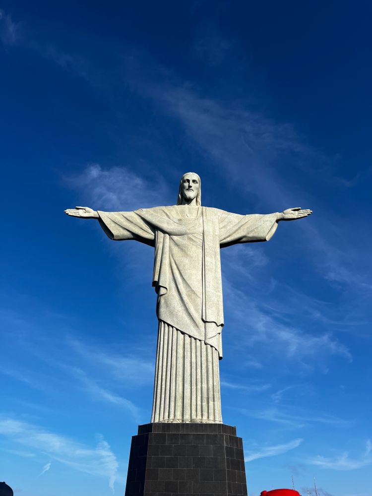 Christ the Redeemer statue in Rio de Janeiro, Brazil, with arms outstretched against a clear blue sky.