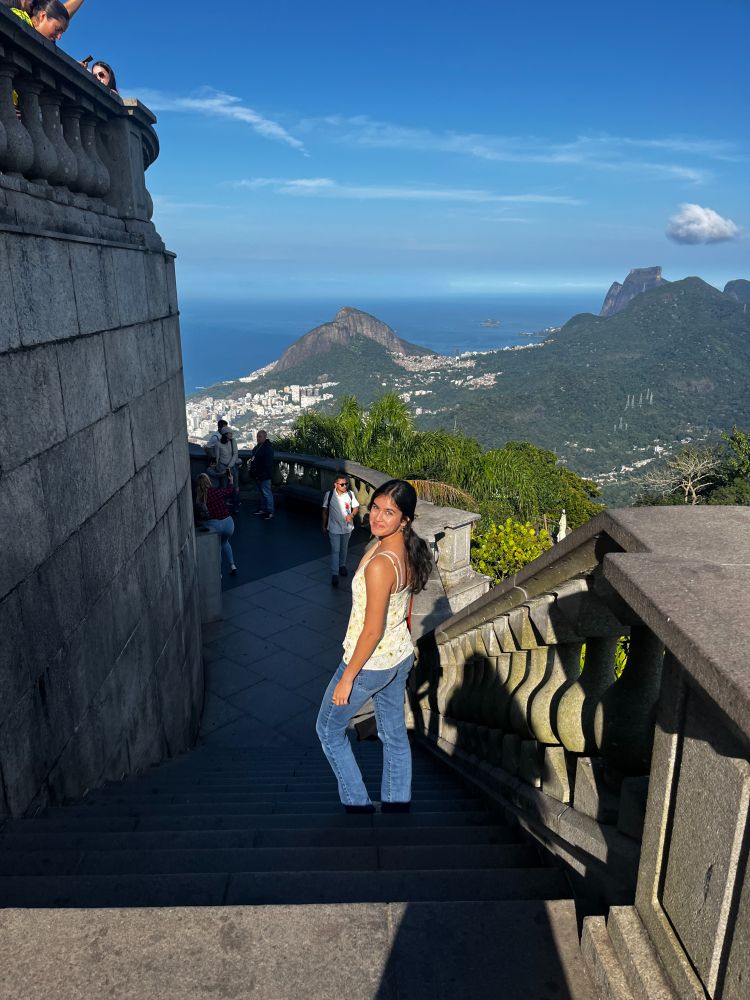 Person standing on the steps of the Christ the Redeemer statue, overlooking the scenic views of Rio de Janeiro's mountains and cityscape.
