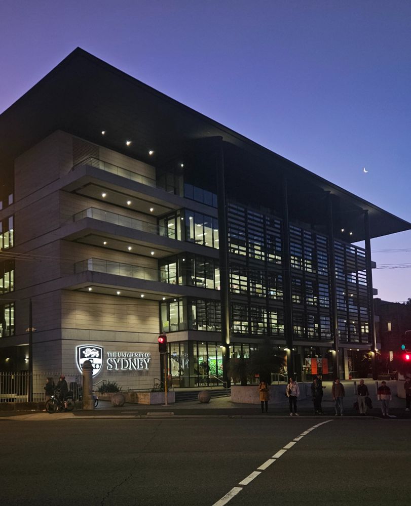 Exterior view of the University of Sydney building at twilight, featuring pedestrians and illuminated signage.