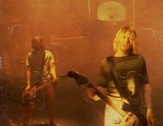 Standbild aus dem Musikvideo zu Nirvanas Smells like Teen Spirit. Die Farben sind in Ocker gehalten, im Vordergrund steht Kurt Cobain mit E-Gitarre und singt.