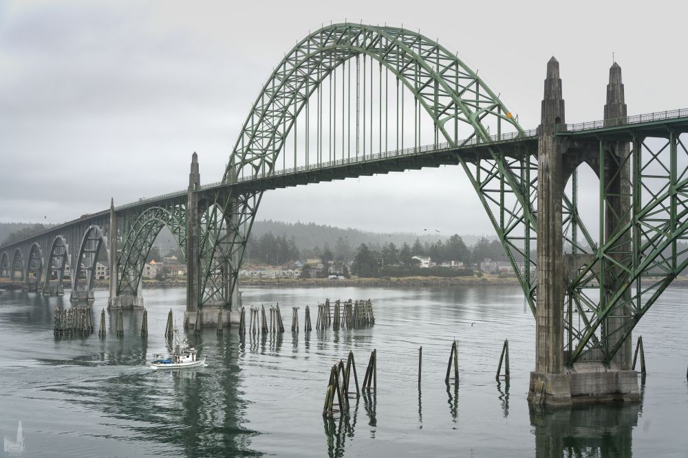 A small fishing vessel heading out to sea passes under the Yaquina Bay Bridge in Newport, Oregon.