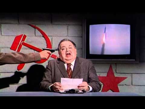 Russian newsreader from the movie Airplane! Reading out the news from a script while a gun is pointed at his head by someone who is standing off camera.