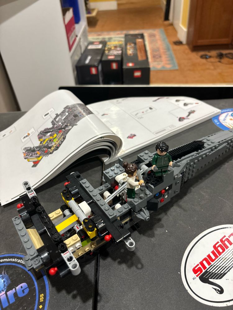 A partially completed Lego model with its assembly manual on a dusty table.