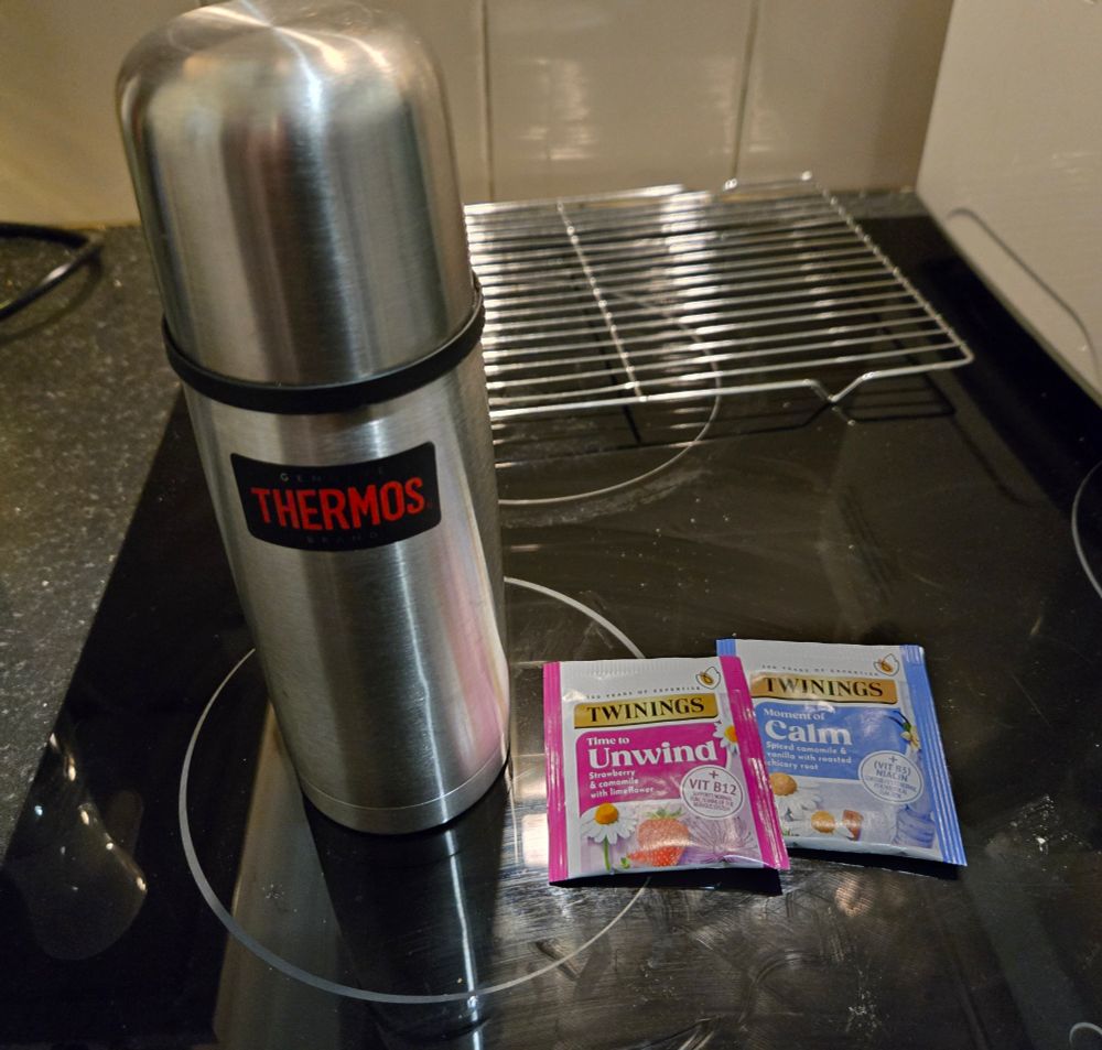 A thermos of coffee and two herbal tea sachets, one labelled 'unwind' and the other 'calm'