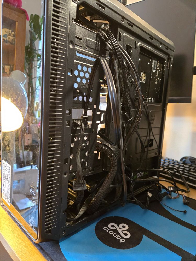 The backside of a pc case, an absolute rats nest of cables hanging out of it