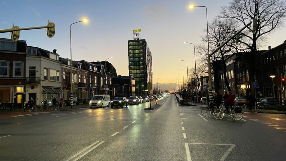 Beautiful sky, looking towards a heavy rain cloud in upcoming dusk. Rush hour in Nijmegen with a queue of cars and some cyclists waiting at the traffic lights of a busy junction.  