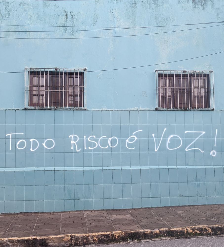 Frase pintada em branco numa parede azul com o texto "todo risco é voz!".