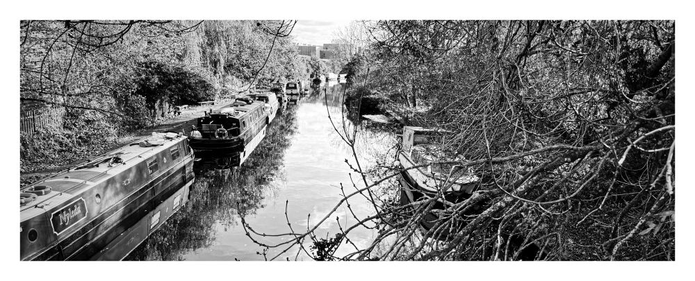 A monochrome photo of some narrowboats along the Grand Union canal in London.
