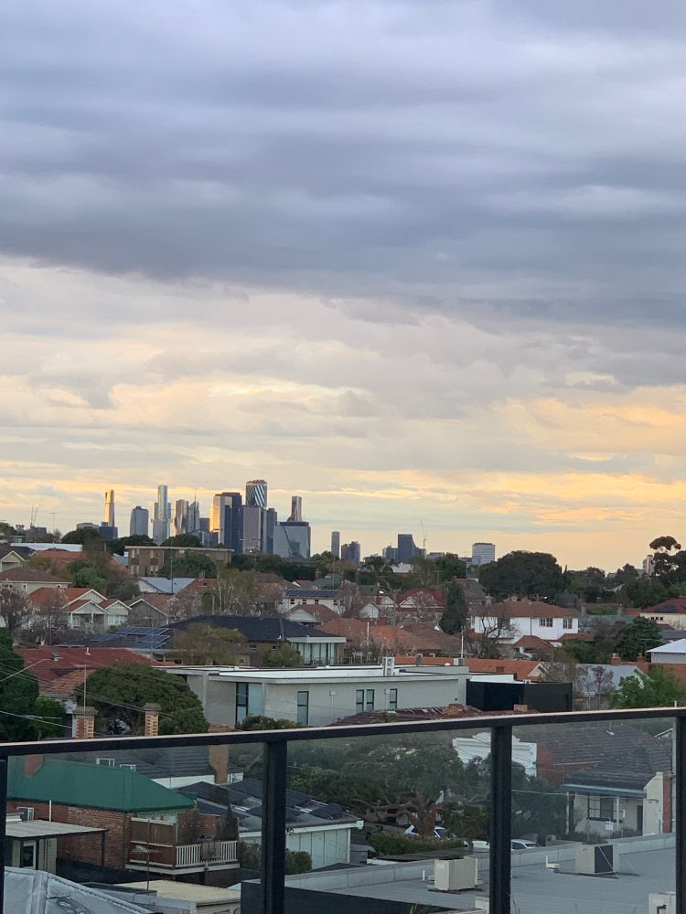A photo of Melbourne CBD with grey, white, yellow and pink clouds