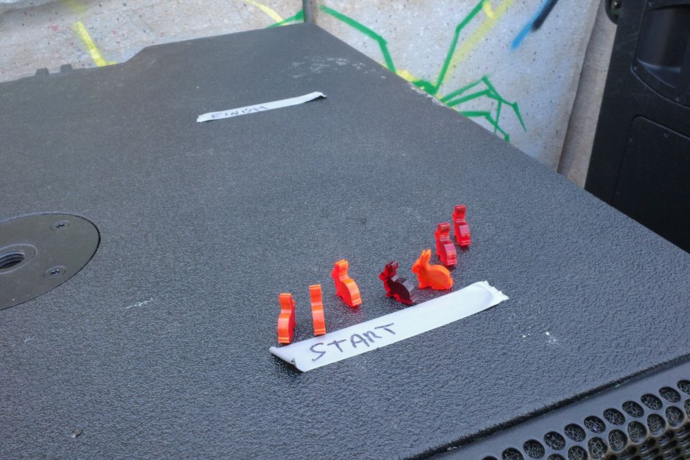 7 red laser cut acrylic rabbits on top of a bass bin. a start and finish line are marked with electrical tape