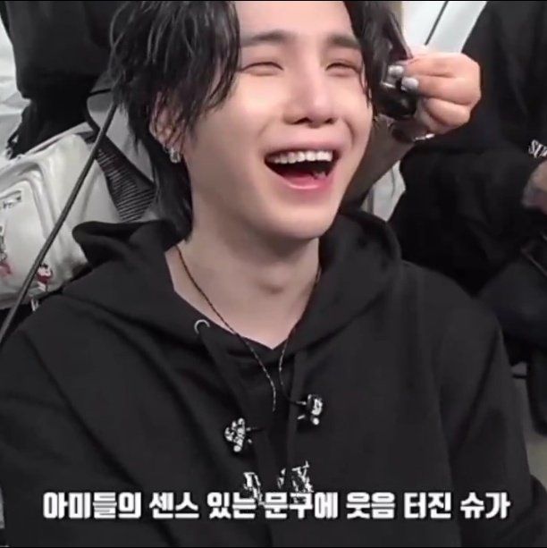 yoongi laughing at the backstage of d-day tour while the staff is fixing his hair. he was reading army posters.