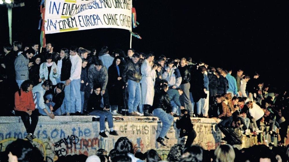 Menschen klettern über die Berliner Mauer als die Grenze zwischen DDR und BRD geöffnet wird