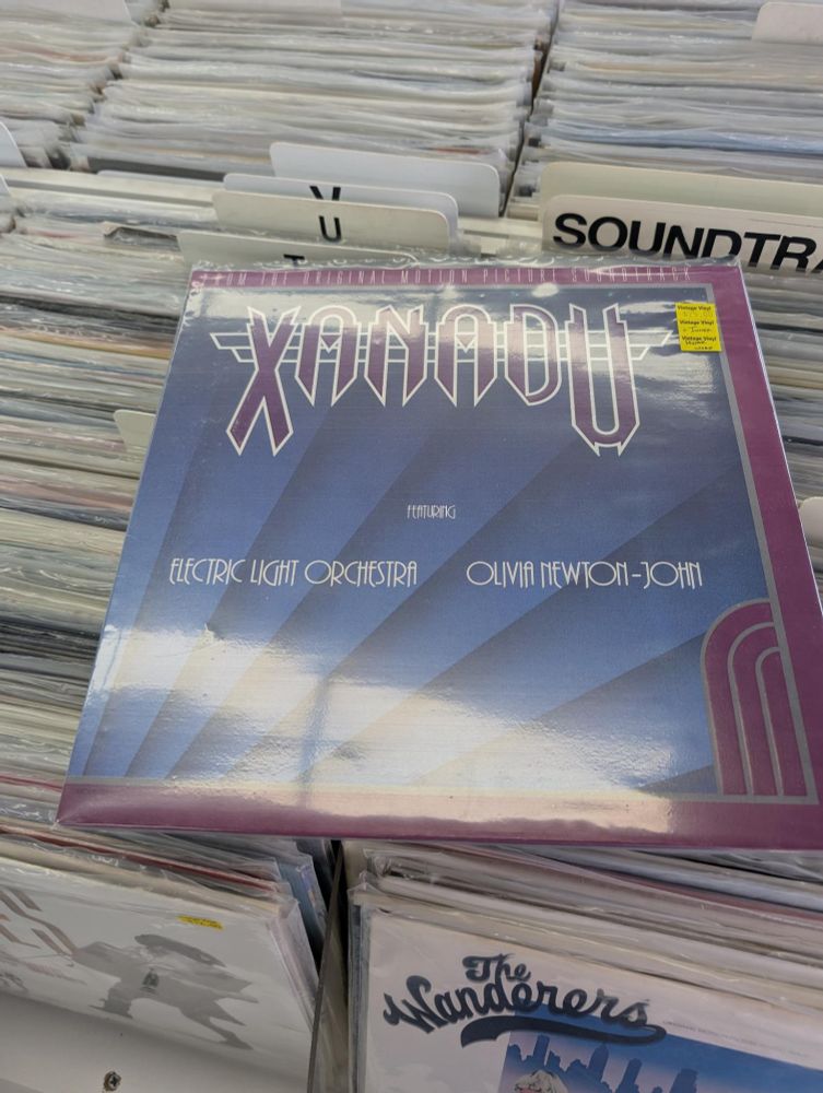 A copy of the original Xanadu motion picture soundtrack on vinyl sitting on top of other vinyl albums in a record store display case.