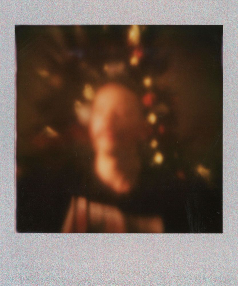 A blurry photo of me with a Christmas tree no the background. Shot on Instax Squre with the gingerbread camera.