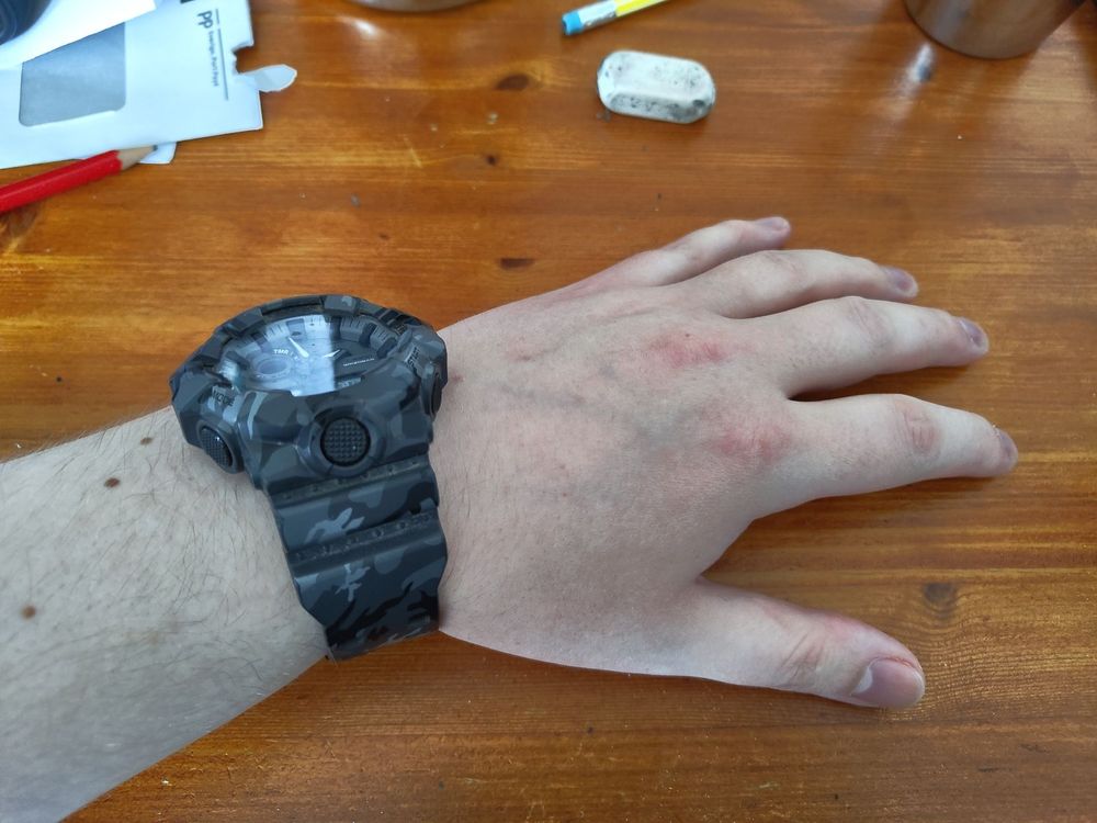 my hand resting on a light brown table. I have a dark gray camo-pattern wristwatch on.