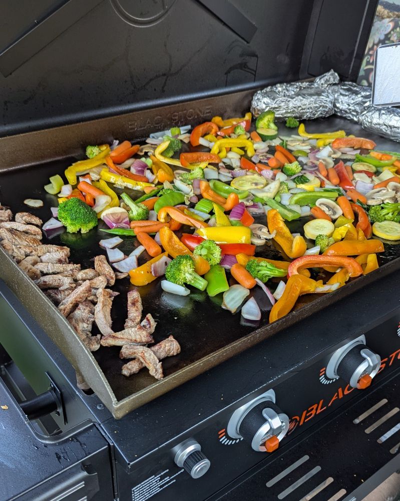 Sirloin steak, red pepper, yellow pepper, orange pepper, green pepper, zucchini, yellow squash, red and white onion, mushrooms and corn-on-the-cobb cooking on the Blackstone griddle. It's way too hot to cook inside today.