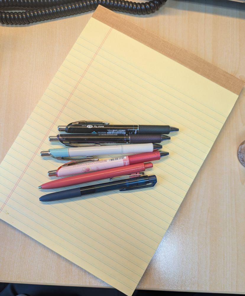 Picture of a blank legal pad with six pens sitting on top of it