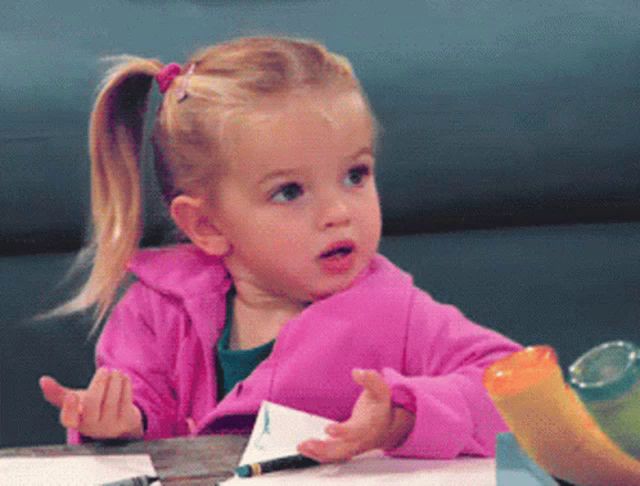 a little girl in a pink jacket sits at a table with a marker