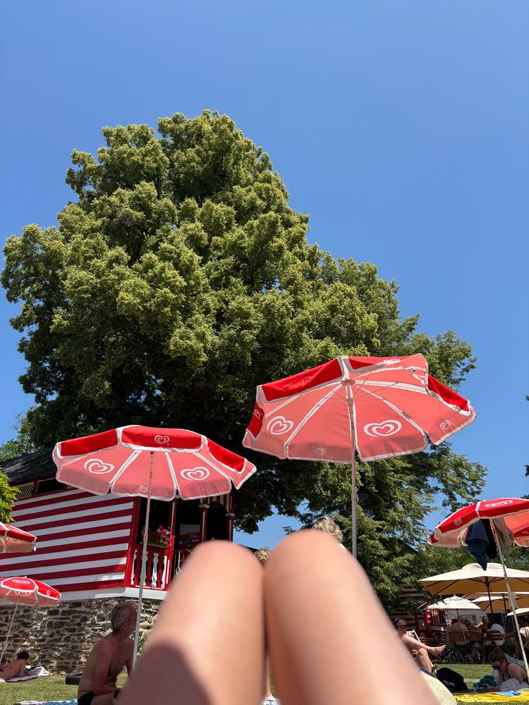 Knie Im Vordergrund, dahinter Sonnenschirme, Bäume, blauer Himmel