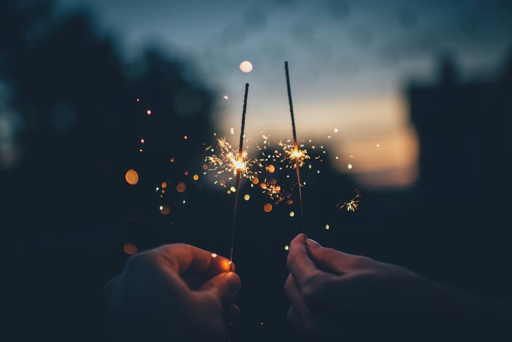 Two people hold lit sparklers against a muted sunset.

Photo by Ian Schneider on Unsplash.
