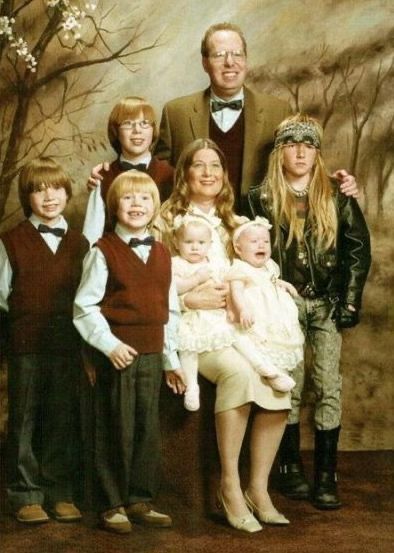 a family portrait of a family of 8 all in preppie clothes except one kid with long hair, in a leather jacket and combat boots