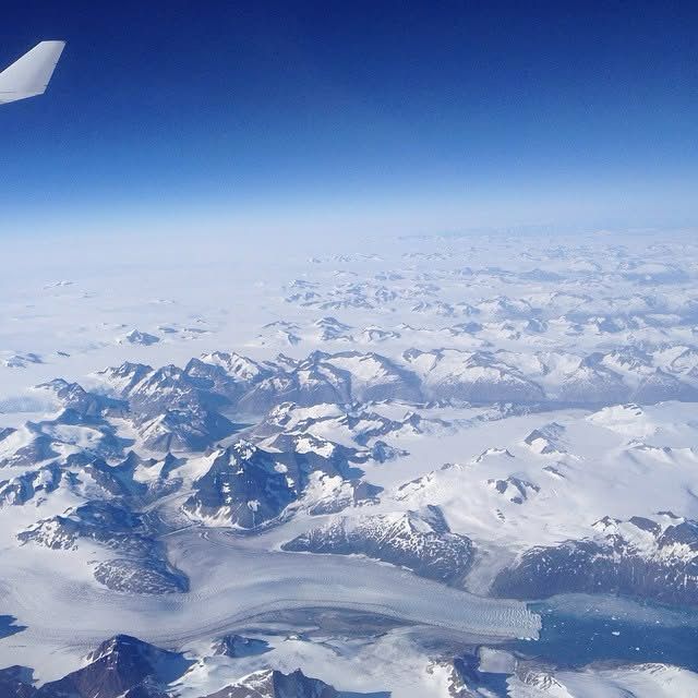 Aerial view of snow-capped mountains and glaciers, seen from an airplane window on a clear day.
