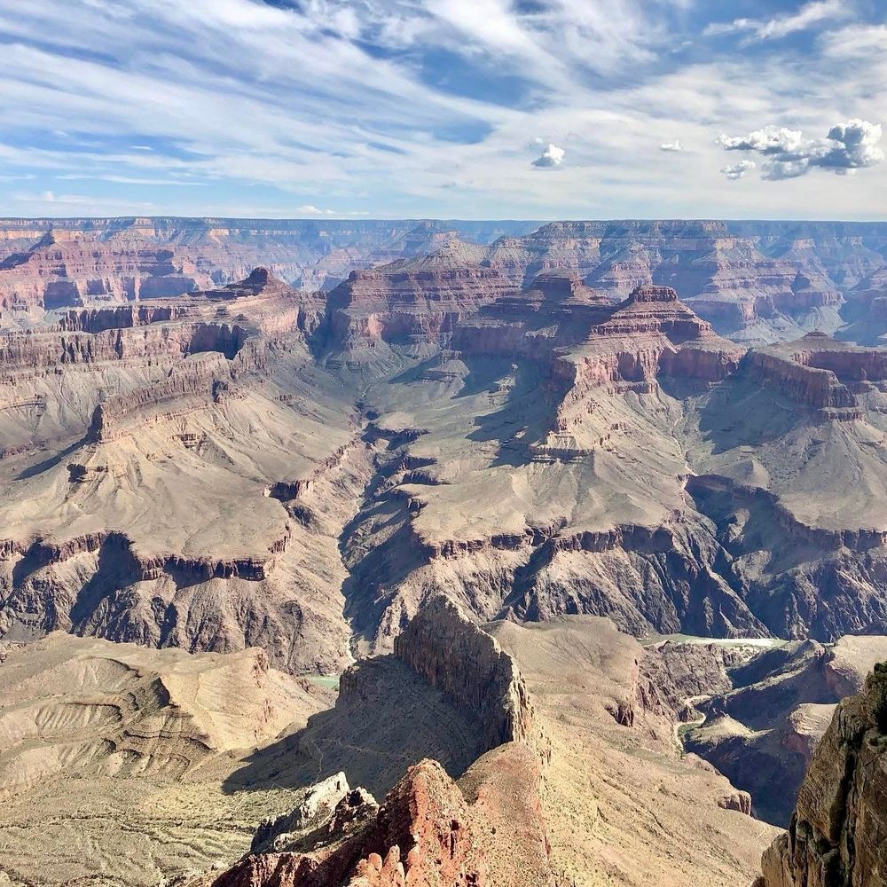 Grand Canyon vista under a blue sky. Layered rock formations create depth and scale.