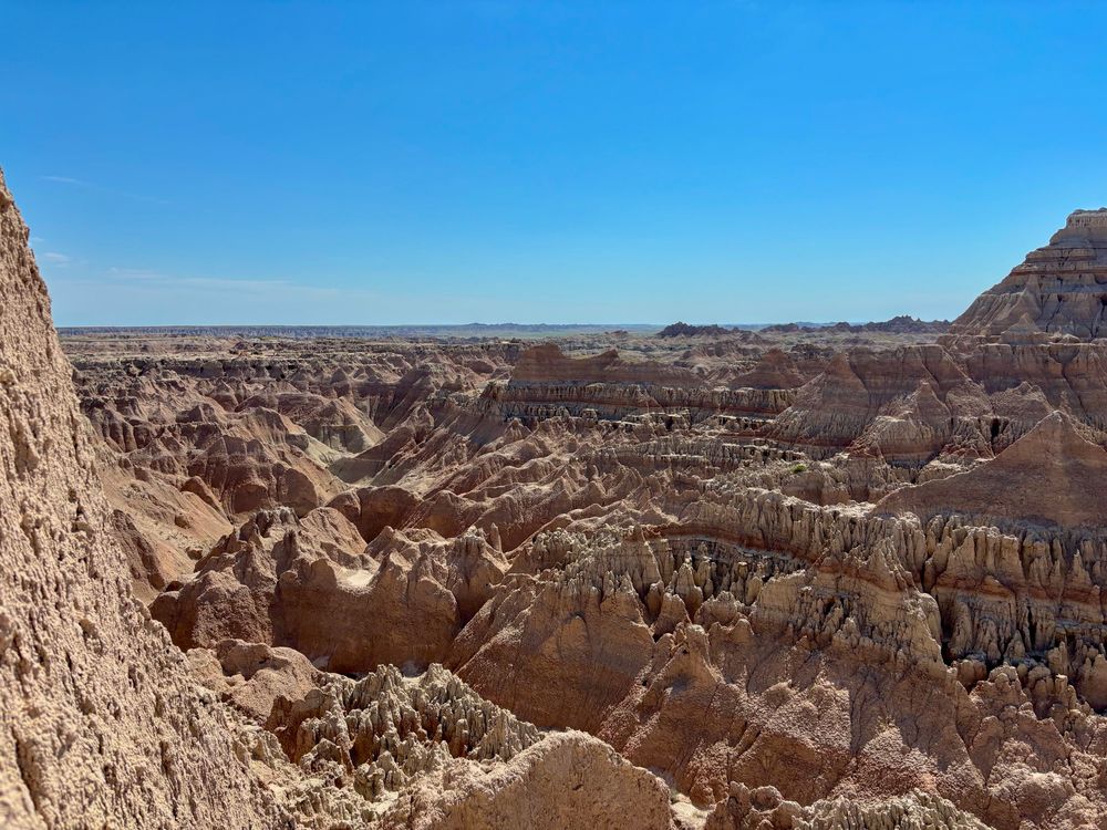 A wide view of a rugged, rocky landscape with layered formations and eroded canyons under a clear blue sky.