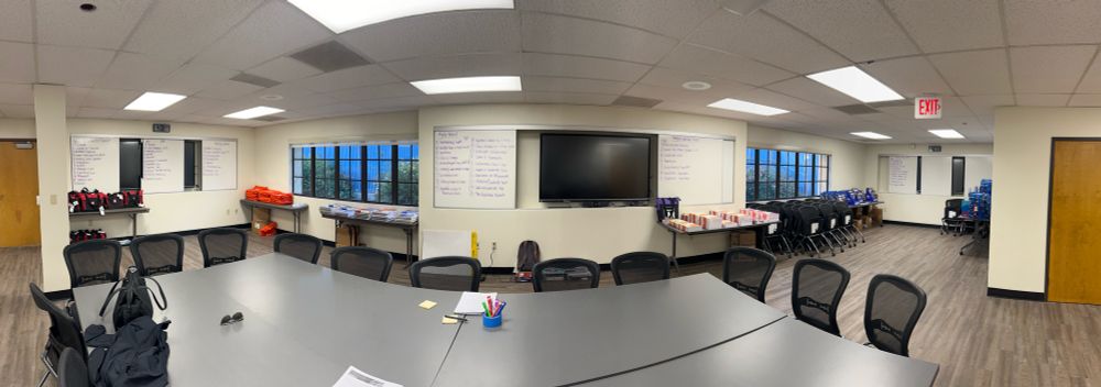 Panorama photo of a room with textbooks organized by publisher and whiteboards with table of contents written. 