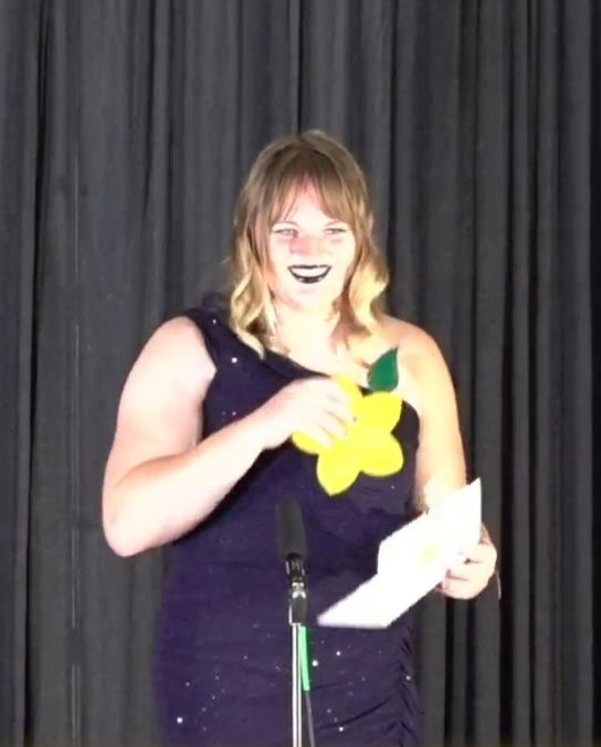 screenshot of frootoon on the stage, her award clutched in her right hand, and the card declaring her the winner in her left. she is in front of the microphone, beaming at the audience, before beginning her speech.