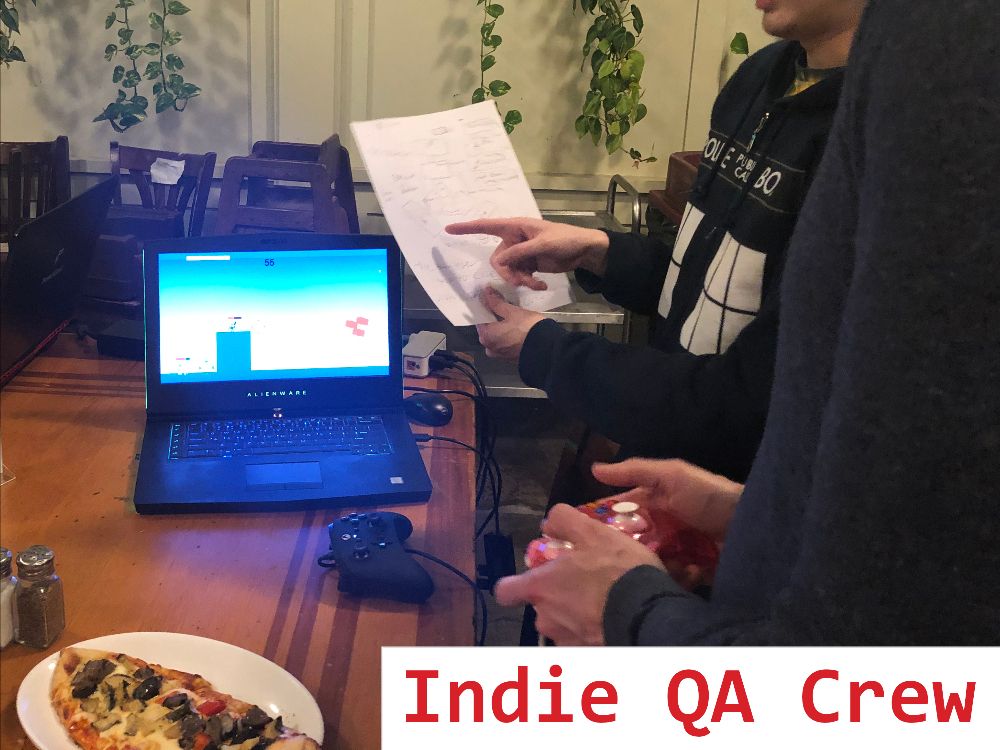 A photo of a couple game devs at one of our IGDA meetups. One is holding a controller and playing a game on a laptop and another is holding a piece of paper that diagrams the game they're working on.