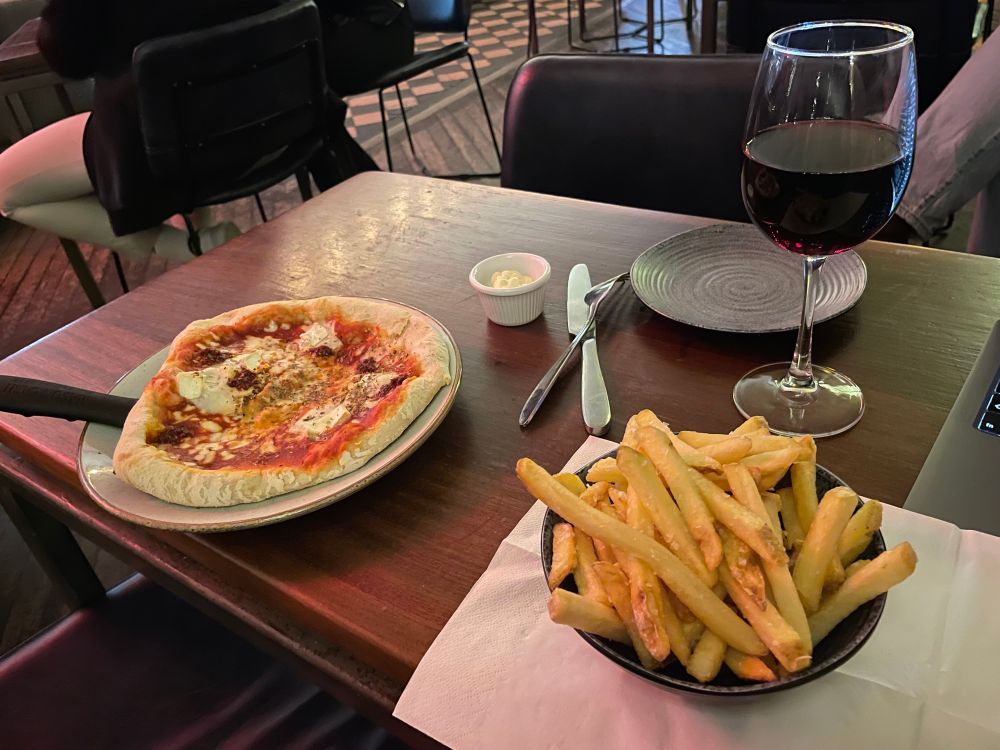A small pizza on a skillet, a bowl of french fries, and a glass of red wine