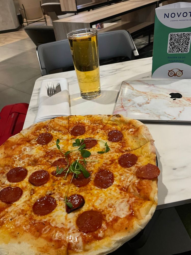 A large pepperoni pizza in front of a laptop and a pint