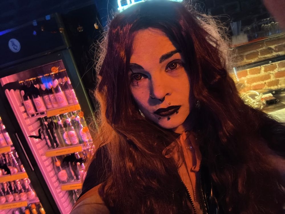 Selfie von mir in Drag mit Langhaarperücke, roten Kontaktlinsen, schwarz roten Lippen, Lackkleid mit Frontreißverschluss und Silikonbrüsten im offenen Ausschnitt 