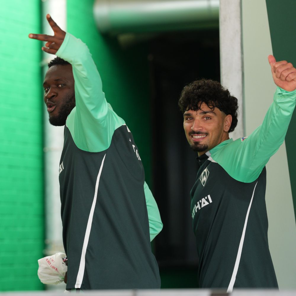 Boniface zeigt Peace-Zeichen und hat eine Rollo-Tüte in der Hand, neben ihm Puertas, der den Daumen hoch macht.