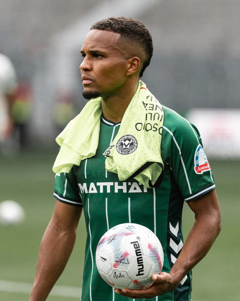 Felix Agu im grünen Heimtrikot hat einen weißen Fußball mit hummel-Aufschrift in der Hand. Um den Hals hat er ein neongelbes Trikot.