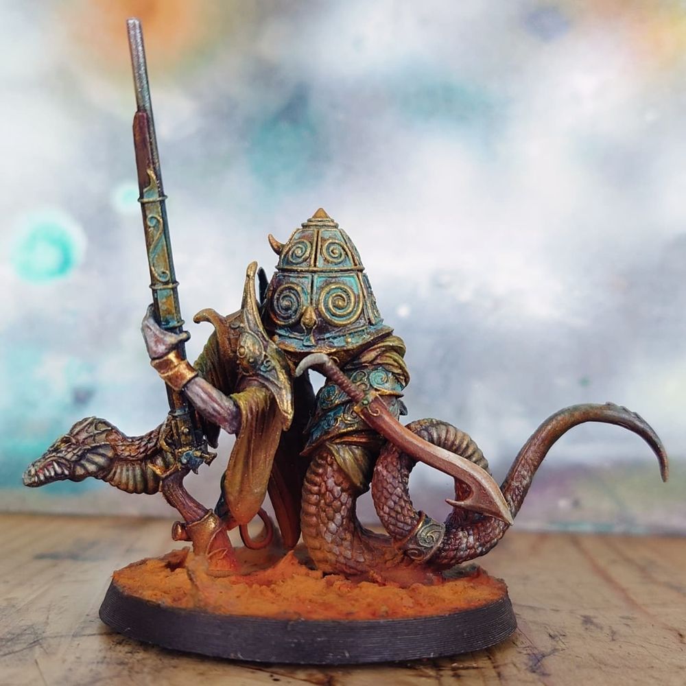 a model in 32mm scale from Rackhamcs Confrontation range: S'Erum the Ophidian. he is a large snake, holding a long musket. an armoured dome rises on his back. His scales have a pattern like a rattlesnake's and he is on a base covered in rusty earth