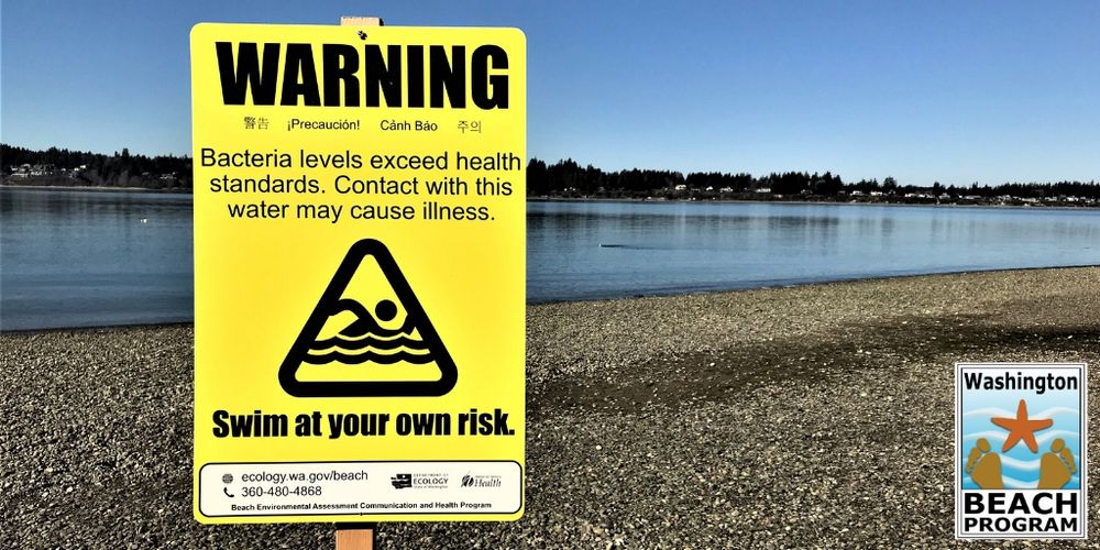 A yellow sign at the beach indicating a closure or advisory.