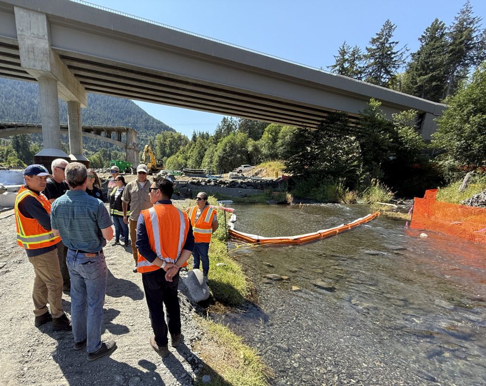 Members of Ecology and the Lower Elwha Klallam Tribe stand near the Indian Creek Confluence, with containment boom deployed in the water in the background during spill response operations.