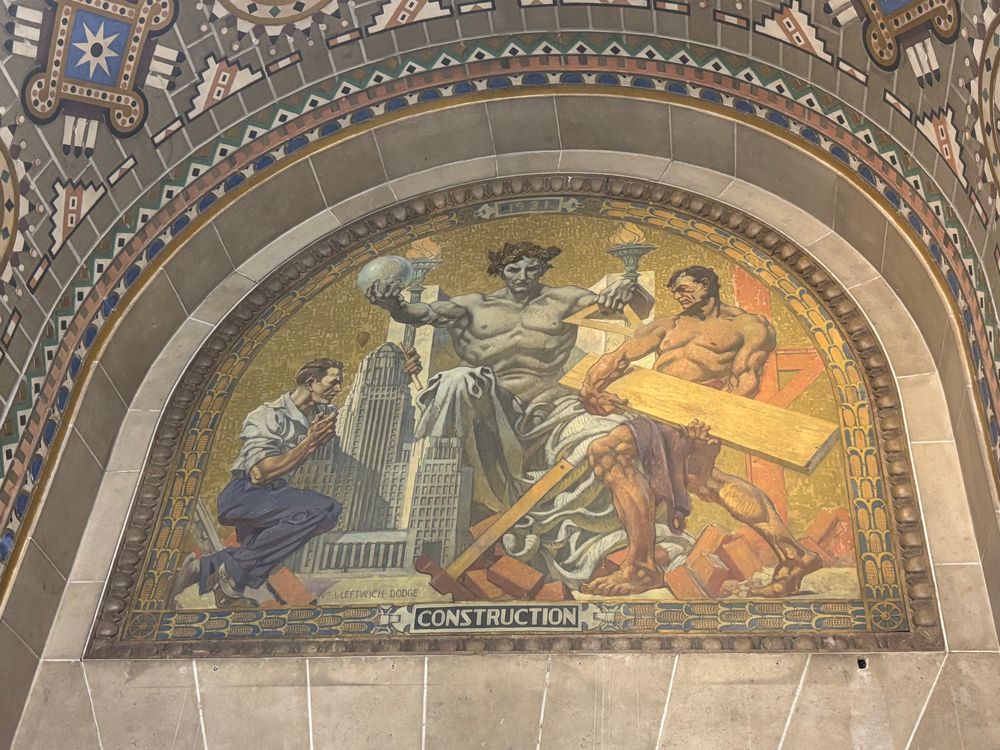 Another mural in Buffalo city hall. Entitled “Construction,” a figure is seated on a throne holding surveying and drafting tools. A figure in front of him steps over piles of bricks and lifts construction materials. To the right of the figure squats the architect of Buffalo city hall,  John J. Wade, working on a model of the building. 