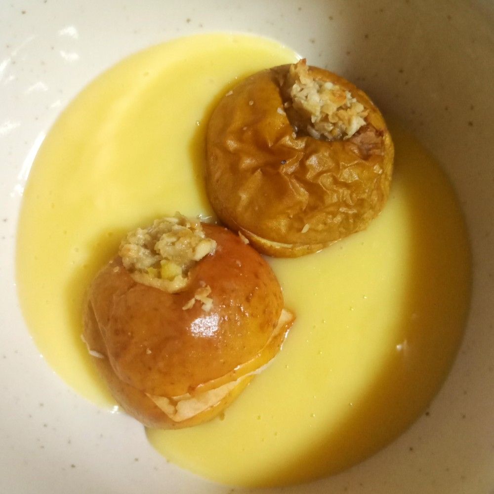 Two baked apples with a flapjack stuffing, in a bowl of custard