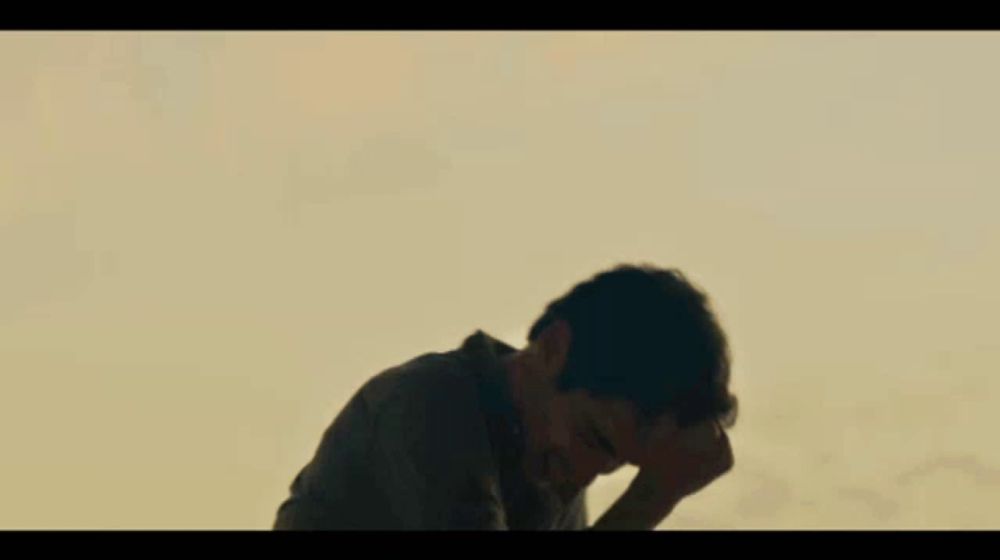 a man covering his face with his hands in front of a mountain