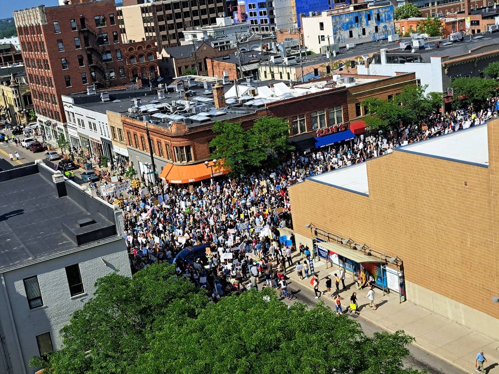 A view of the No Kings Day protest in Ann Arbor, MI. This perspective is at the top of the 4th Street parking garage. Protesters fill the street in front of the federal building. Many of the protesters are outside the view of this picture.