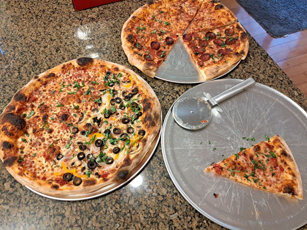 Three trays of NY style pizza slices with various toppings. Some cheese, some pepperoni, and some with mushroom, onion, bell pepper, and olives