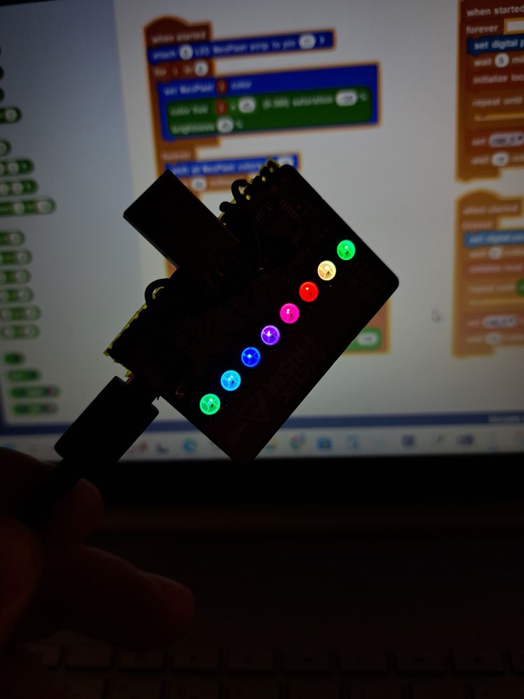 Me holding the test board in front of my computer monitor. The LEDs on the board are lit up in a rainbow pattern.
